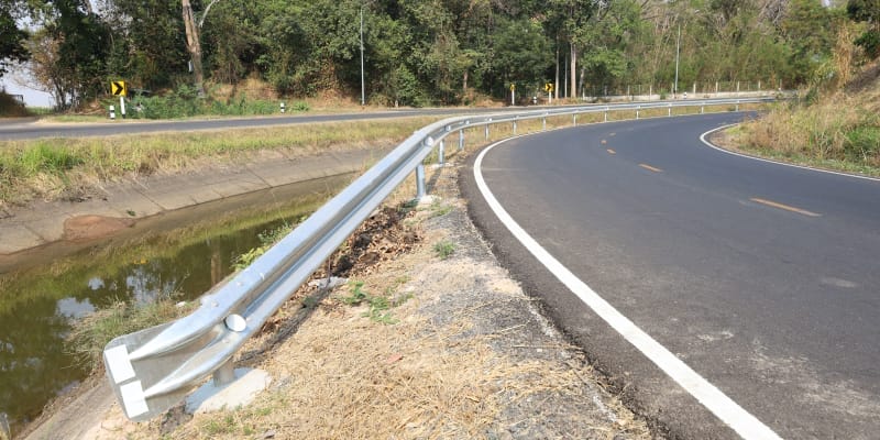 A metal road crash barrier installed along the edge of a paved roadway to ensure highway safety, illustrating the importance of choosing the right barrier for site conditions.